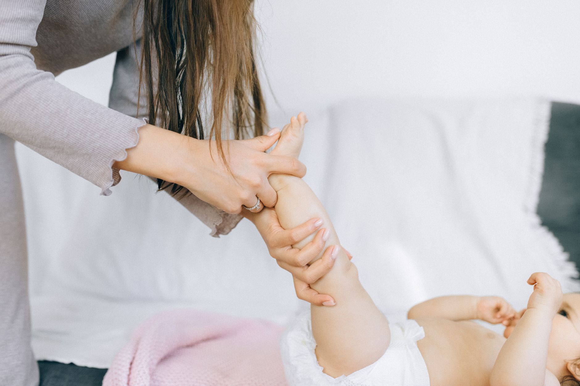 An adult massaging a baby&rsquo;s leg and foot on a white bed. Stock photograph.