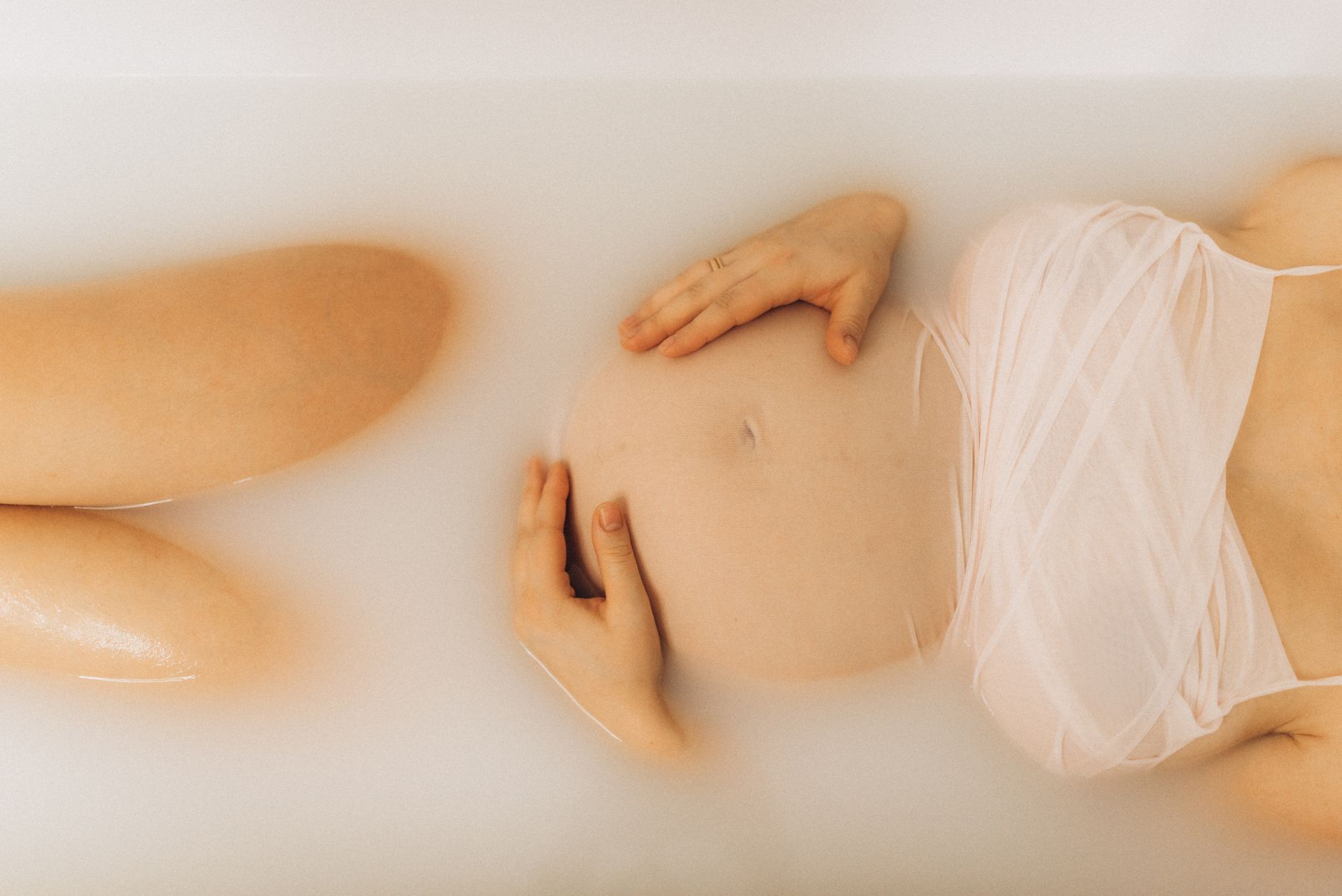 A pregnant woman resting in a warm bath, hands on her belly. Stock photograph.