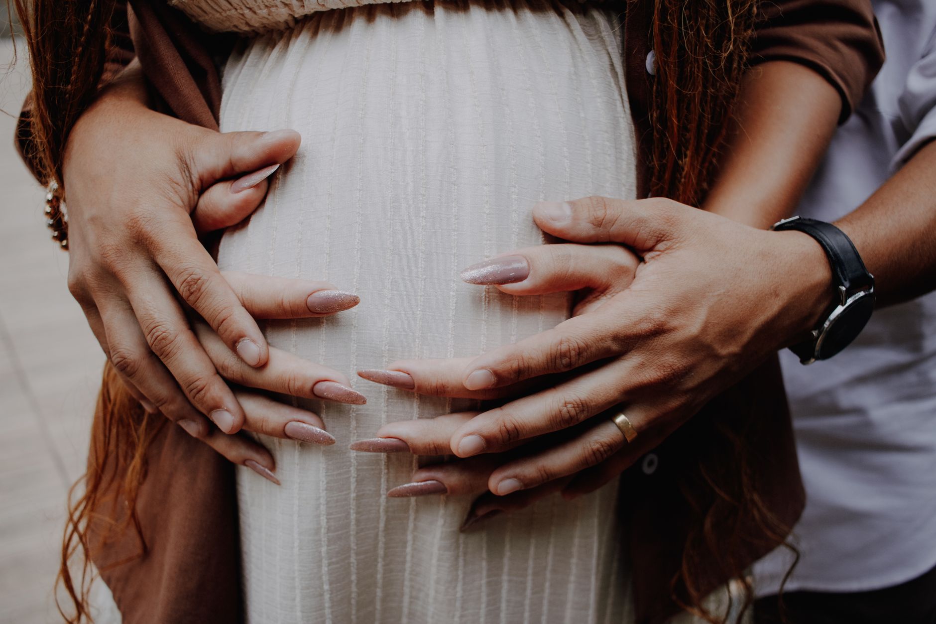 Close view of two pairs of hands resting on a pregnant belly. Stock photograph.