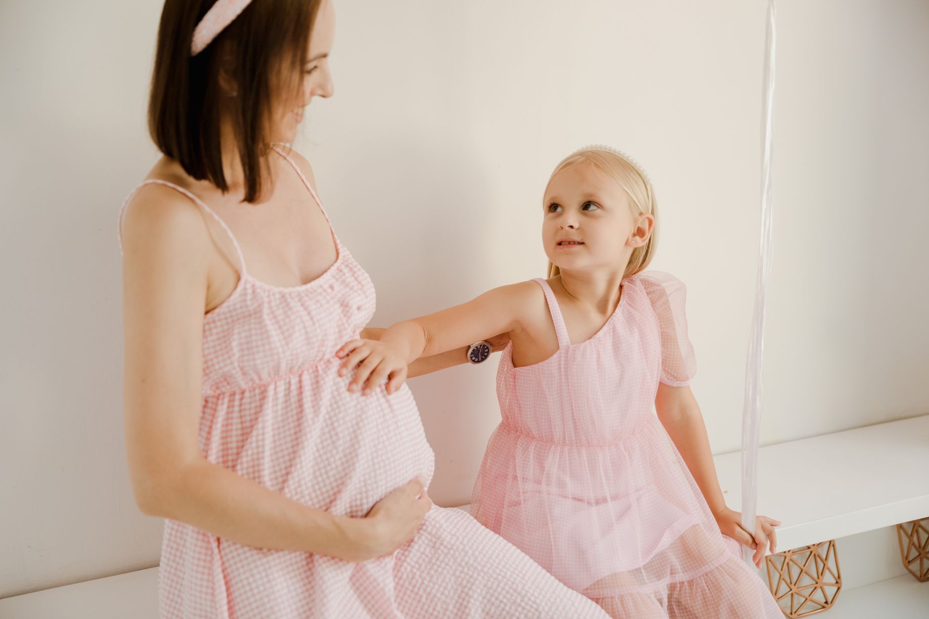 A young girl resting her hand on her pregnant mother&rsquo;s belly. Stock photograph.